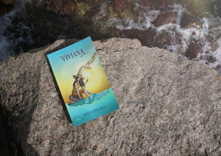 Kinderbuch auf Felsen im Wasser mit Buchcover Illustration einer Hexe mit Zauberstab am Meer